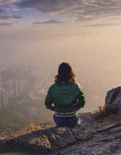 Woman sitting on rock in hills above Hong Kong looking down over the city.